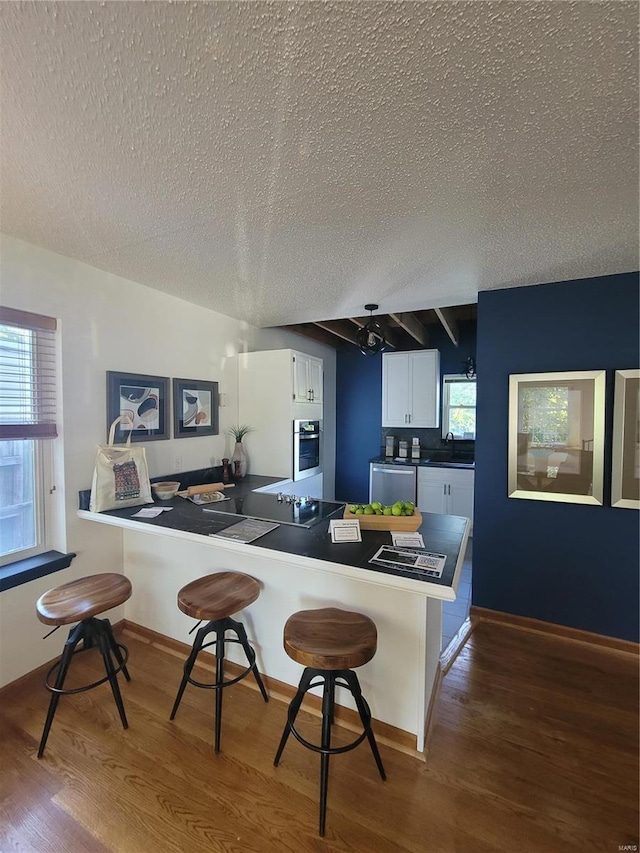 kitchen featuring appliances with stainless steel finishes, white cabinetry, a kitchen breakfast bar, kitchen peninsula, and dark wood-type flooring