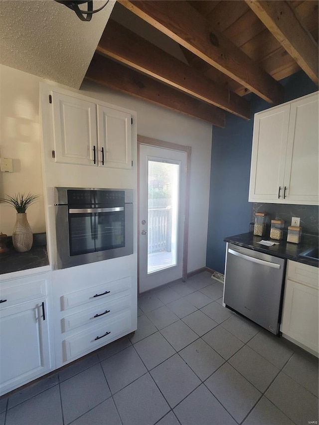 kitchen with white cabinetry, appliances with stainless steel finishes, light tile patterned flooring, and beam ceiling