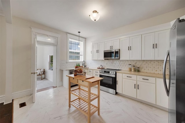 kitchen with white cabinetry, decorative backsplash, stainless steel appliances, and hanging light fixtures