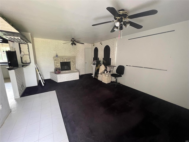 exercise area with ceiling fan, brick wall, light tile patterned floors, and a brick fireplace