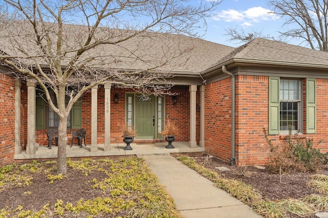 entrance to property featuring a porch, roof with shingles, and brick siding