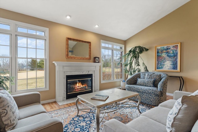 living room with baseboards, a high end fireplace, vaulted ceiling, light wood-type flooring, and recessed lighting