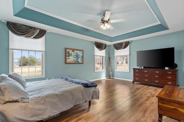 bedroom with a tray ceiling, crown molding, baseboards, and wood finished floors