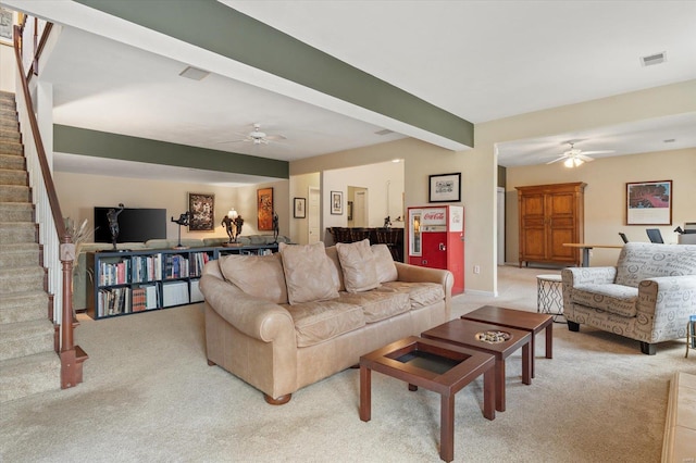 living area featuring light carpet, visible vents, ceiling fan, stairway, and beamed ceiling