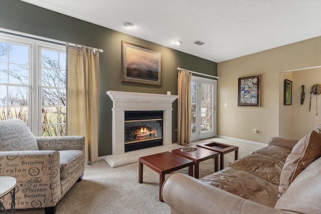 living area with baseboards, a glass covered fireplace, visible vents, and light colored carpet