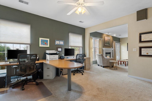 office space featuring light colored carpet, a glass covered fireplace, visible vents, and baseboards