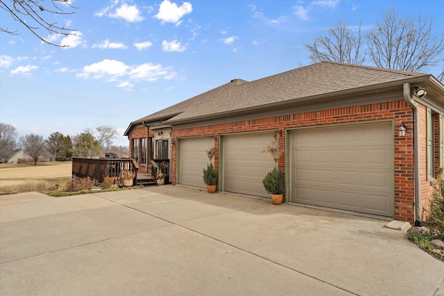 view of side of property featuring a shingled roof, a deck, concrete driveway, and brick siding