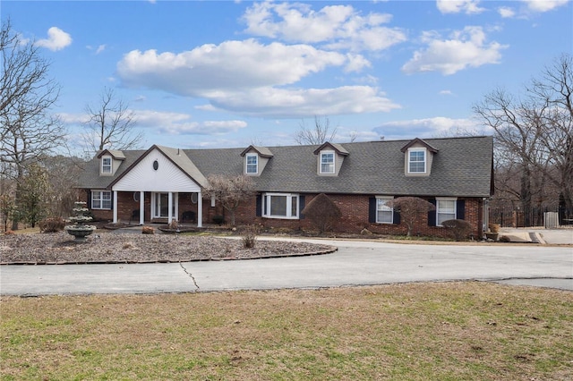 new england style home featuring brick siding, a front yard, and a shingled roof