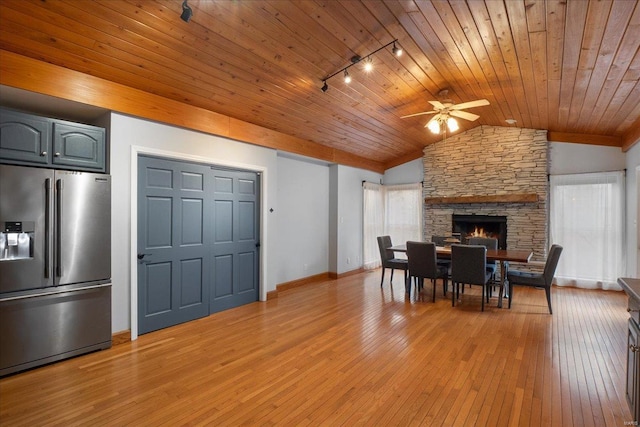 dining room featuring light hardwood / wood-style flooring, track lighting, a stone fireplace, vaulted ceiling, and wooden ceiling