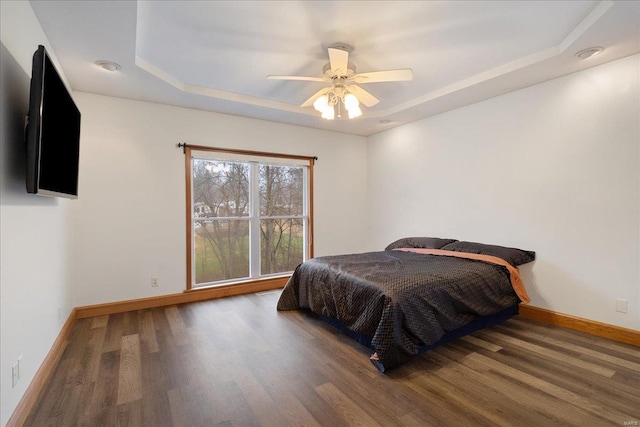 bedroom with dark hardwood / wood-style floors, a raised ceiling, and ceiling fan