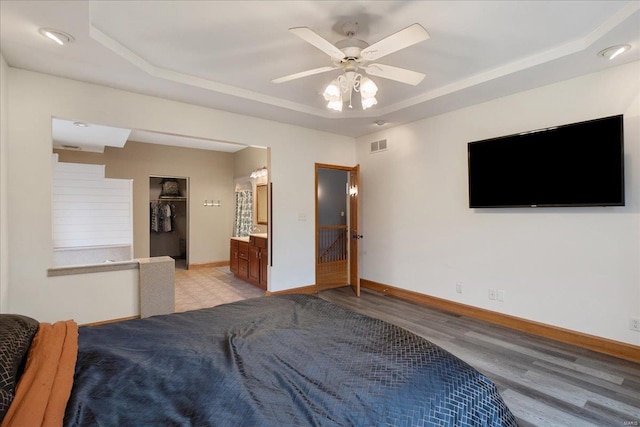 bedroom with a raised ceiling, connected bathroom, ceiling fan, and light hardwood / wood-style flooring