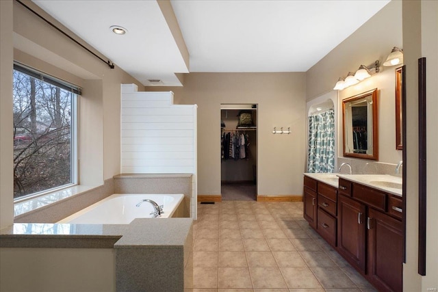 bathroom with a relaxing tiled tub, a healthy amount of sunlight, and vanity