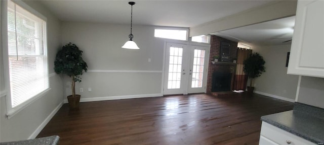 unfurnished dining area featuring dark wood-style floors, french doors, vaulted ceiling with beams, a brick fireplace, and baseboards