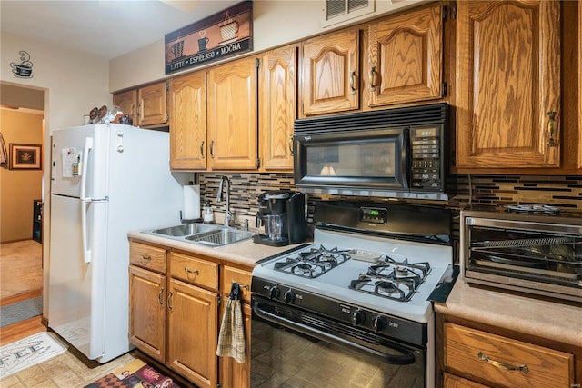 kitchen featuring tasteful backsplash, gas range oven, sink, and white fridge