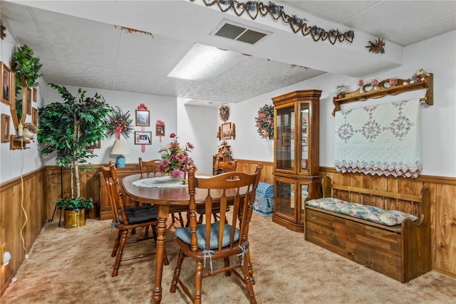 carpeted dining space featuring a paneled ceiling and wooden walls