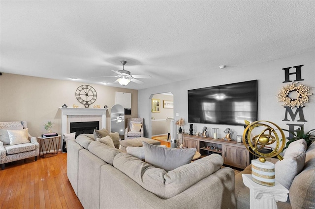 living room featuring a tile fireplace, ceiling fan, a textured ceiling, and light hardwood / wood-style floors