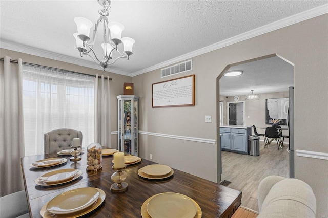 dining area featuring crown molding, a chandelier, a textured ceiling, and light wood-type flooring