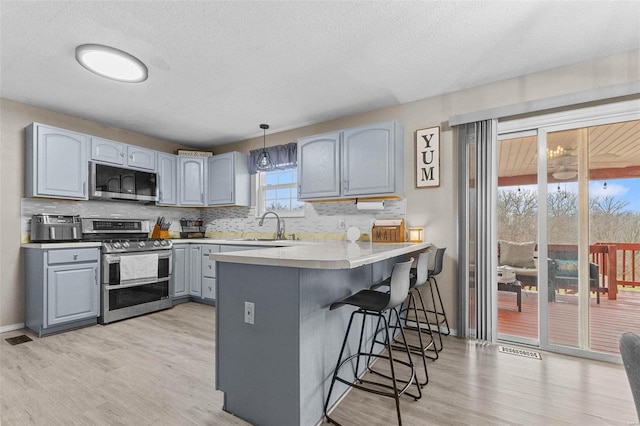 kitchen with gray cabinetry, appliances with stainless steel finishes, a kitchen breakfast bar, kitchen peninsula, and pendant lighting