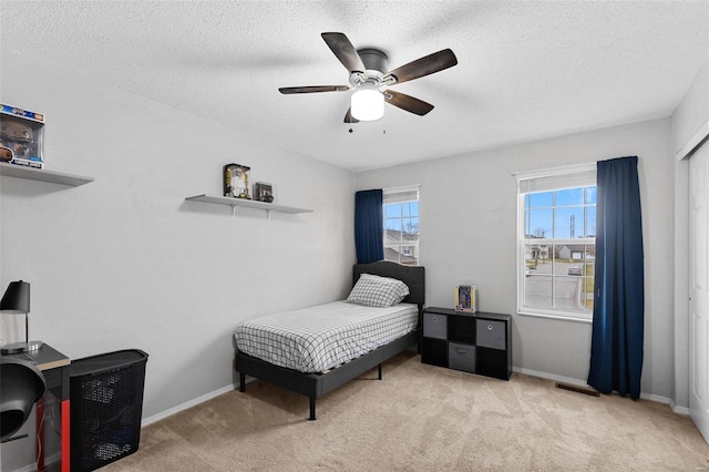 bedroom with ceiling fan, light carpet, and a textured ceiling