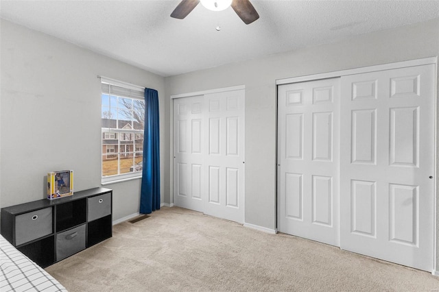 carpeted bedroom featuring ceiling fan, a textured ceiling, and two closets