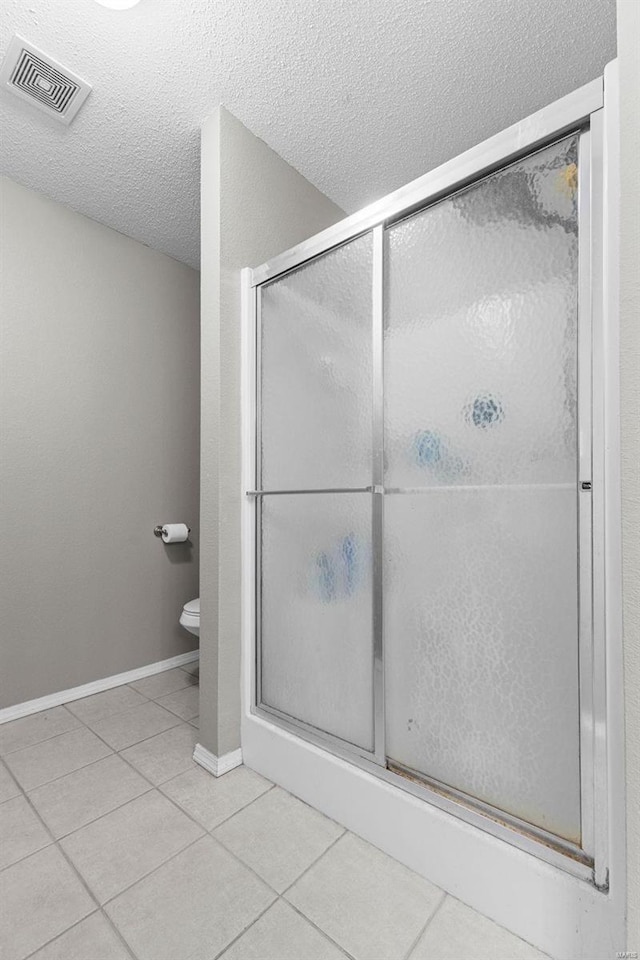 bathroom featuring tile patterned flooring, a shower with shower door, toilet, and a textured ceiling