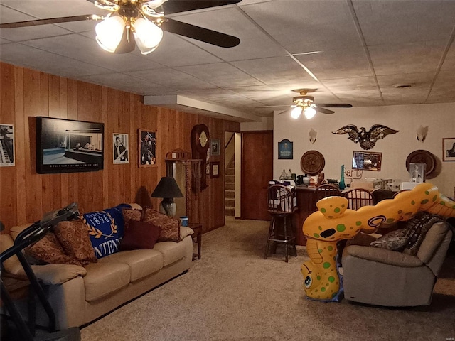 carpeted living room featuring wooden walls and ceiling fan