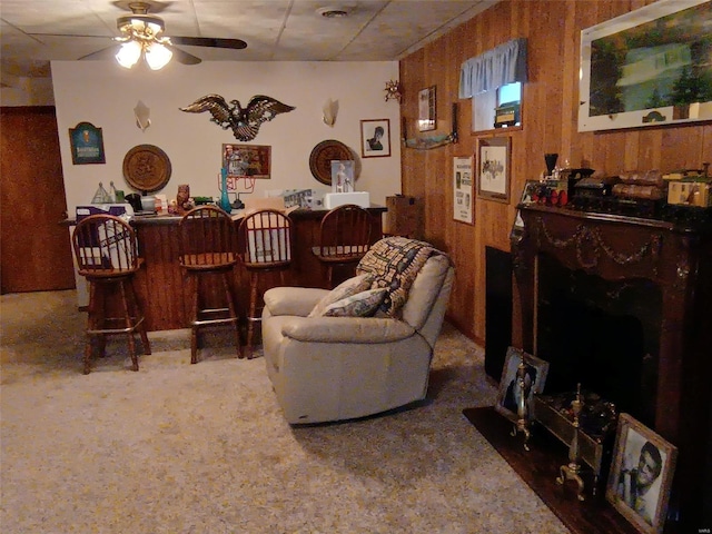 carpeted living room featuring wooden walls, ceiling fan, and indoor bar