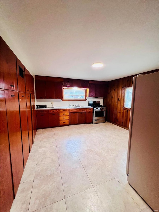 kitchen featuring stainless steel gas range, sink, wood walls, refrigerator, and light tile patterned floors