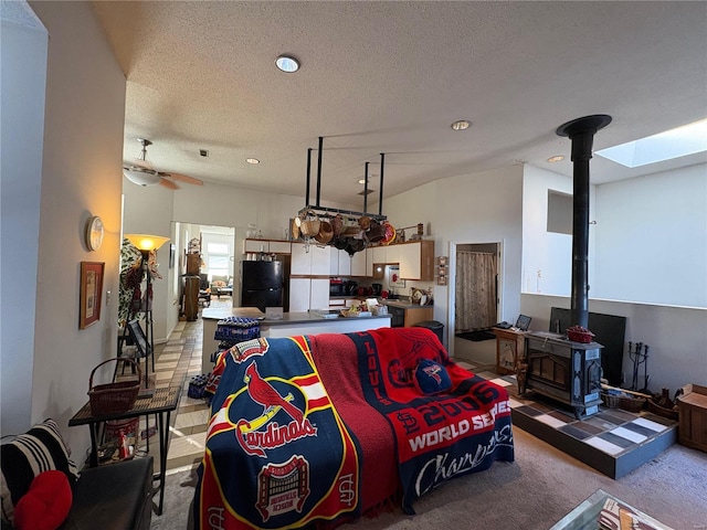 carpeted living room featuring ceiling fan, a skylight, a textured ceiling, and a wood stove