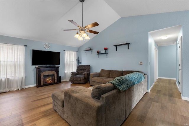 living room featuring vaulted ceiling, a glass covered fireplace, wood finished floors, and a ceiling fan