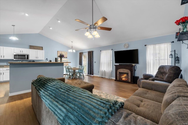 living area featuring a ceiling fan, wood finished floors, high vaulted ceiling, a warm lit fireplace, and baseboards