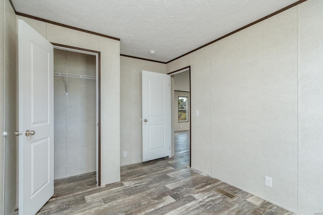 unfurnished bedroom featuring a textured ceiling, wood finished floors, visible vents, ornamental molding, and a closet