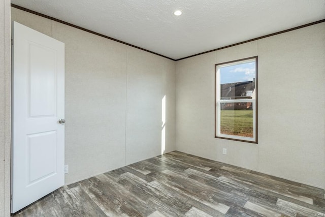 empty room featuring a textured ceiling, ornamental molding, and wood finished floors