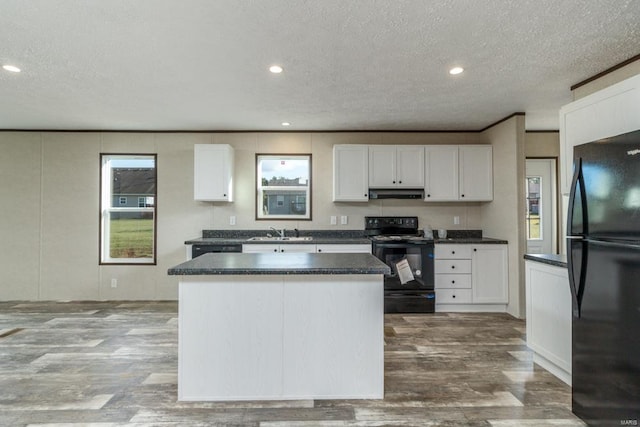 kitchen featuring under cabinet range hood, wood finished floors, a kitchen island, a sink, and black appliances