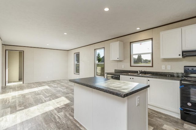 kitchen with black range with electric stovetop, dark countertops, a sink, and light wood-style floors