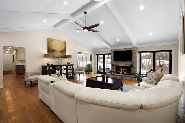 living area with a ceiling fan, lofted ceiling with beams, dark wood-type flooring, a stone fireplace, and recessed lighting