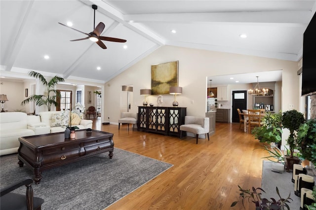 living room with vaulted ceiling with beams, a wealth of natural light, wood finished floors, and ceiling fan with notable chandelier