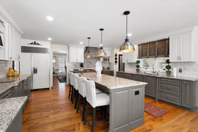 kitchen featuring a center island, decorative light fixtures, light wood-style flooring, white cabinets, and built in appliances