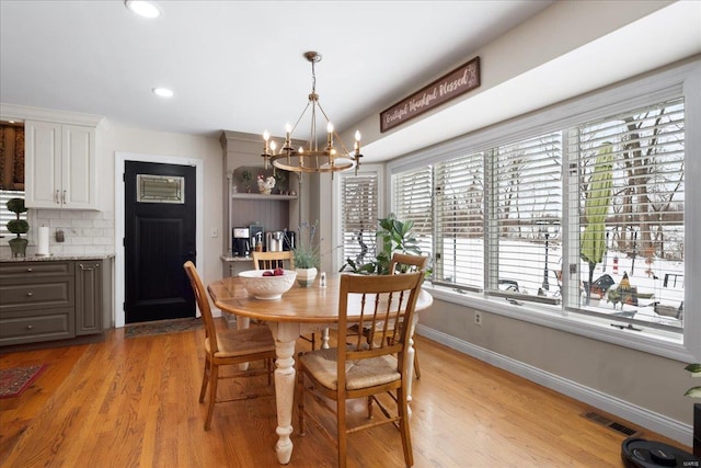 dining space featuring an inviting chandelier, baseboards, visible vents, and light wood finished floors