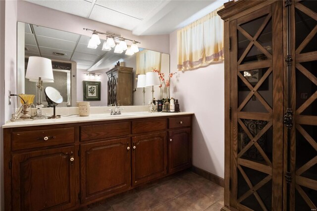 bathroom with vanity, baseboards, a drop ceiling, and tile patterned floors