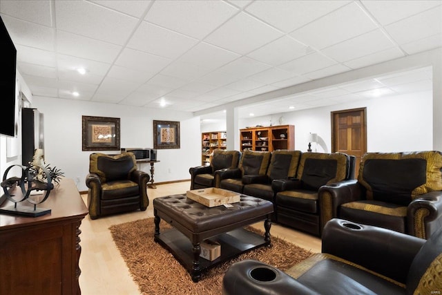 living area featuring a paneled ceiling, baseboards, and light wood finished floors