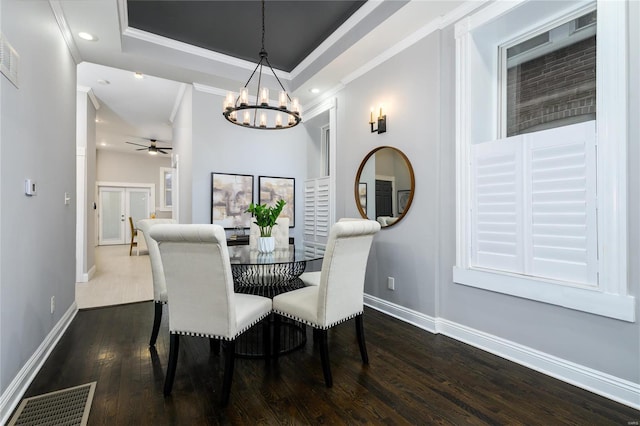 dining room with dark hardwood / wood-style flooring, a tray ceiling, ceiling fan with notable chandelier, and crown molding