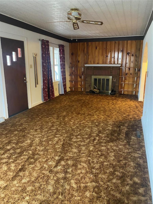 unfurnished living room with ceiling fan, a fireplace, dark carpet, and wood walls