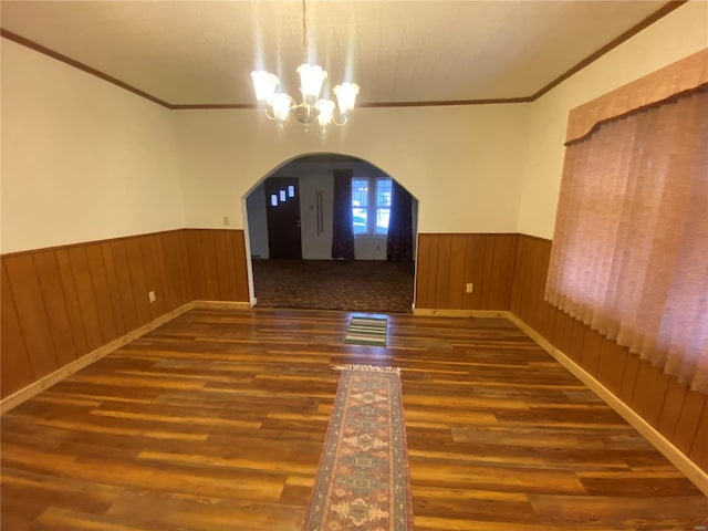 spare room with crown molding, dark hardwood / wood-style floors, a chandelier, and wood walls