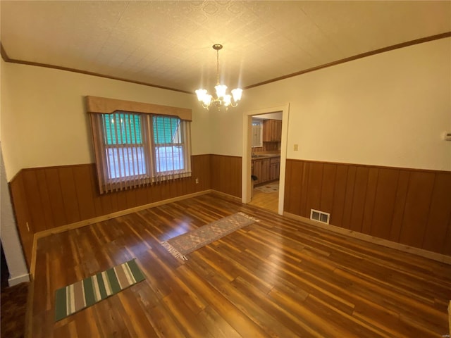 unfurnished dining area with crown molding, wooden walls, dark hardwood / wood-style floors, and a chandelier