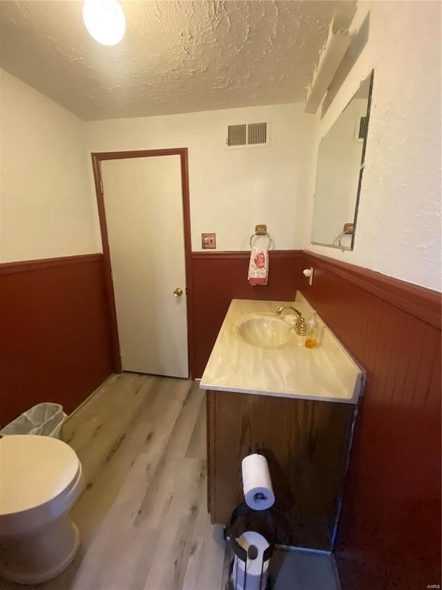 bathroom featuring toilet, wood-type flooring, a textured ceiling, vanity, and wooden walls