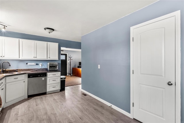 kitchen featuring dark countertops, light wood-style flooring, stainless steel dishwasher, white cabinetry, and a sink