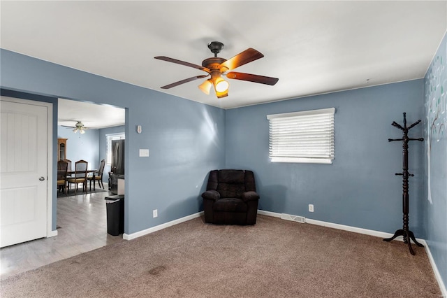 living area with carpet flooring, ceiling fan, visible vents, and baseboards