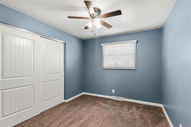 unfurnished bedroom featuring baseboards, visible vents, ceiling fan, dark colored carpet, and a closet