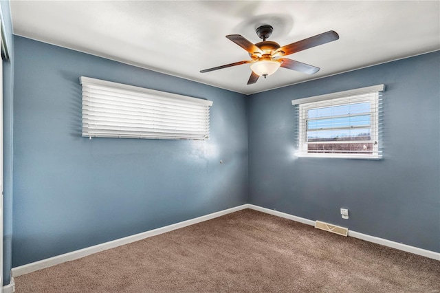 carpeted empty room with baseboards, visible vents, and a ceiling fan